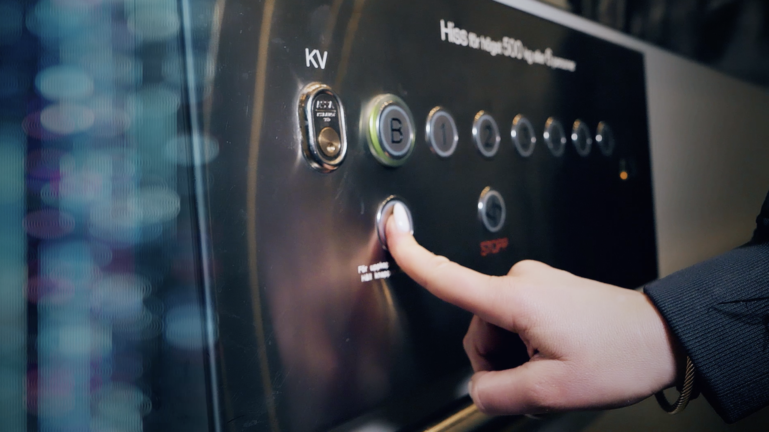 A finger pressing the emergency alarm button on a lift control panel.